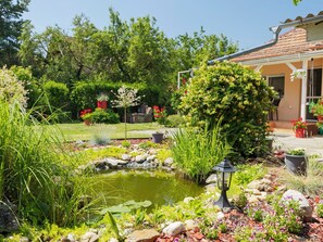Un giardino con uno stagno, diverse piante e un edificio con un tetto in tegole.