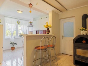 Una cucina con forno integrato, un'area pranzo con sedie in metallo, una finestra con tende e una pianta in vaso.