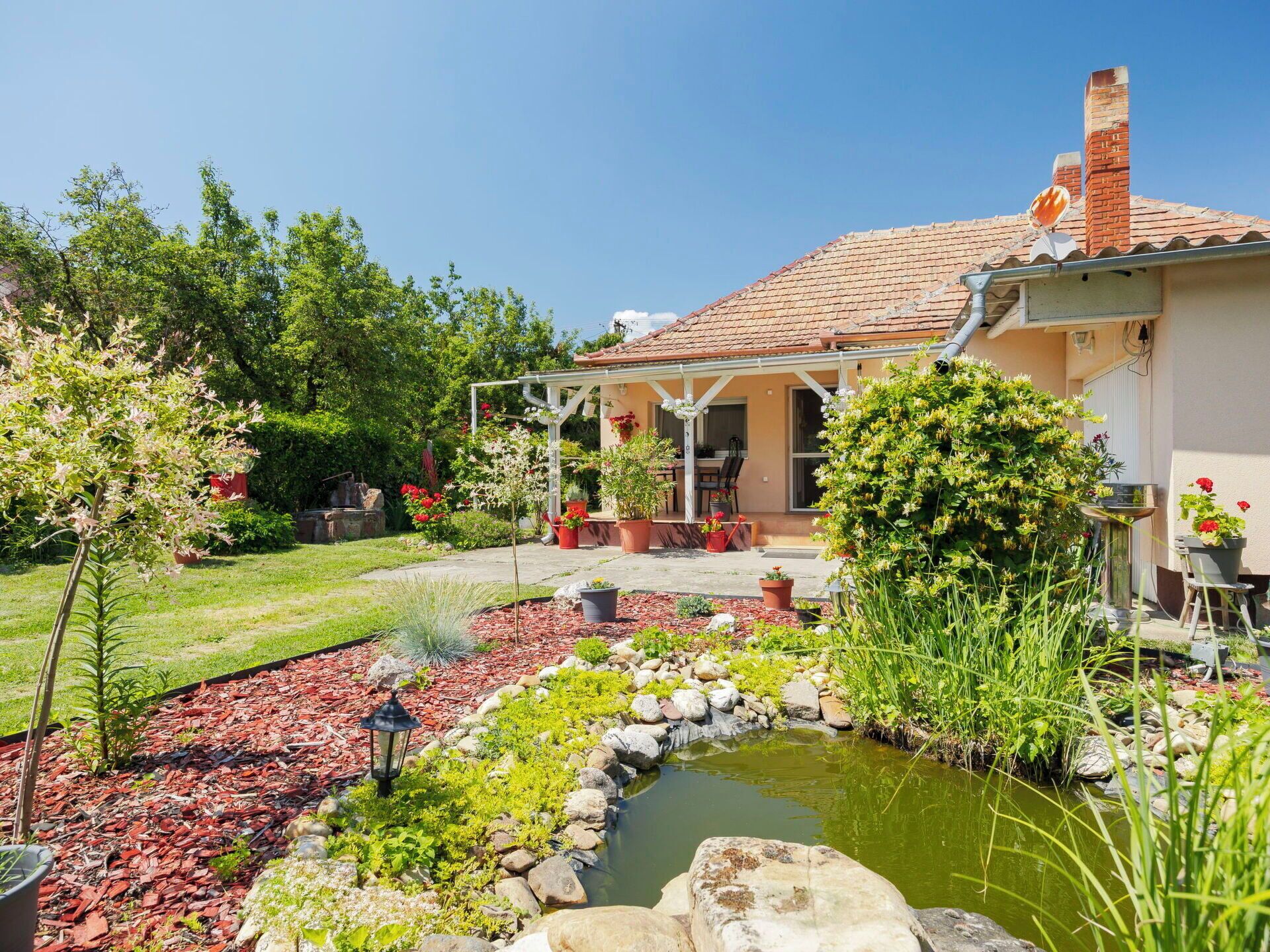 Una casa con jardín, patio y un pequeño estanque.