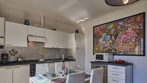 A modern kitchen with white cabinets, a dining table set with plates and glasses, and a colorful abstract painting on the wall. - Nice apartment for 4 people with WIFI, TV, balcony, pets allowed and panoramic view (Gravedona)