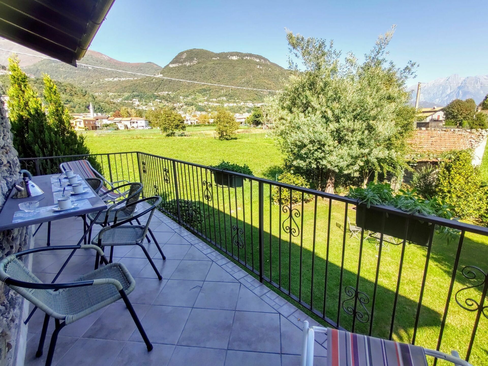 Een balkon met een eettafel, stoelen en uitzicht op een groen landschap met bomen en bergen.