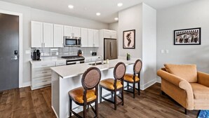 A modern kitchen with white cabinets, a central island with bar stools, a microwave, and a refrigerator. - Luxury 2 Bed 2 Bath Condo In Bywater with Pool! (New Orleans)