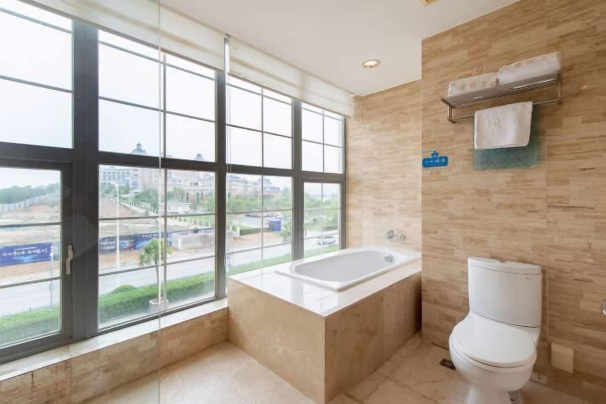 A modern bathroom with a large window, a bathtub, and a toilet.