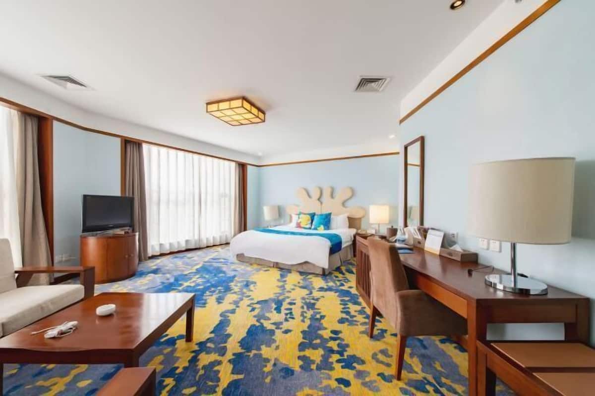 A hotel room with a bed, a desk, a chair, a TV, and a lamp.