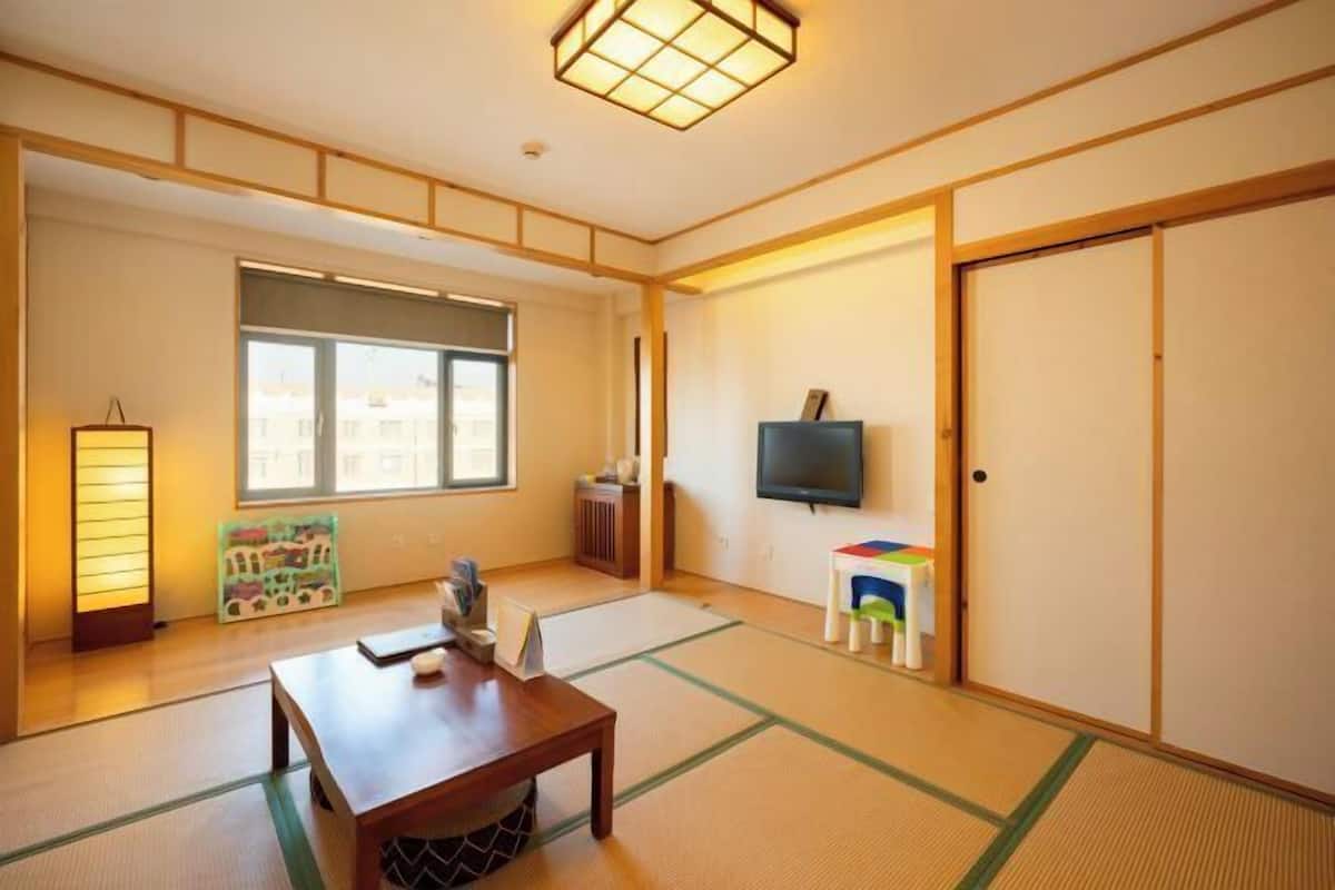 A traditional Japanese room with tatami flooring, a low wooden table, a television, and a sliding door.