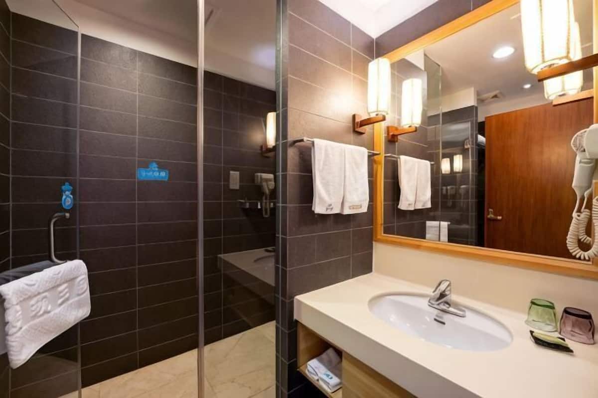 A modern bathroom with a glass shower enclosure, a sink with a mirror, and a hairdryer on the wall.