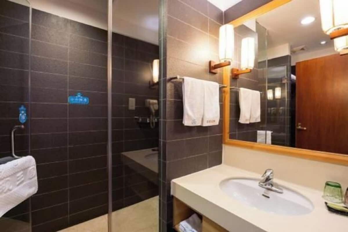 A modern bathroom with a glass shower enclosure, a white sink, and a large mirror with a wooden frame.