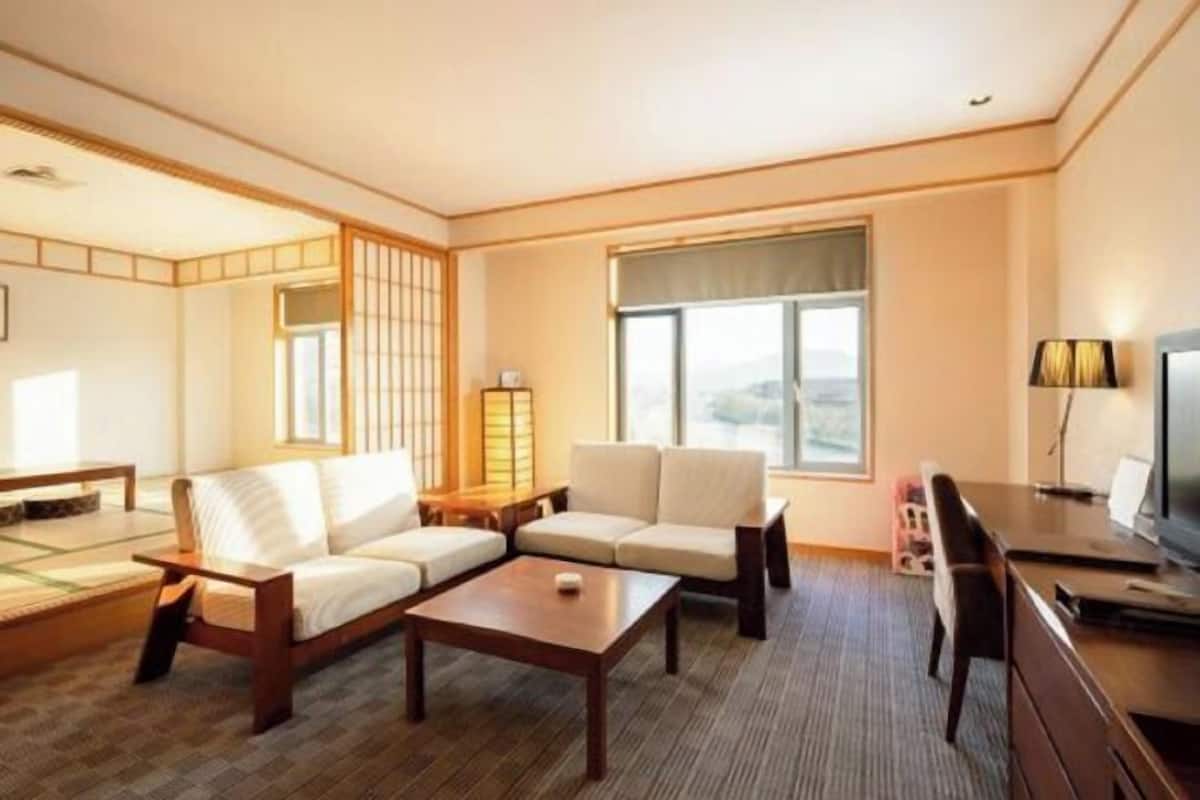 A hotel room with a sofa set, a coffee table, a TV, and a large window offering a view.