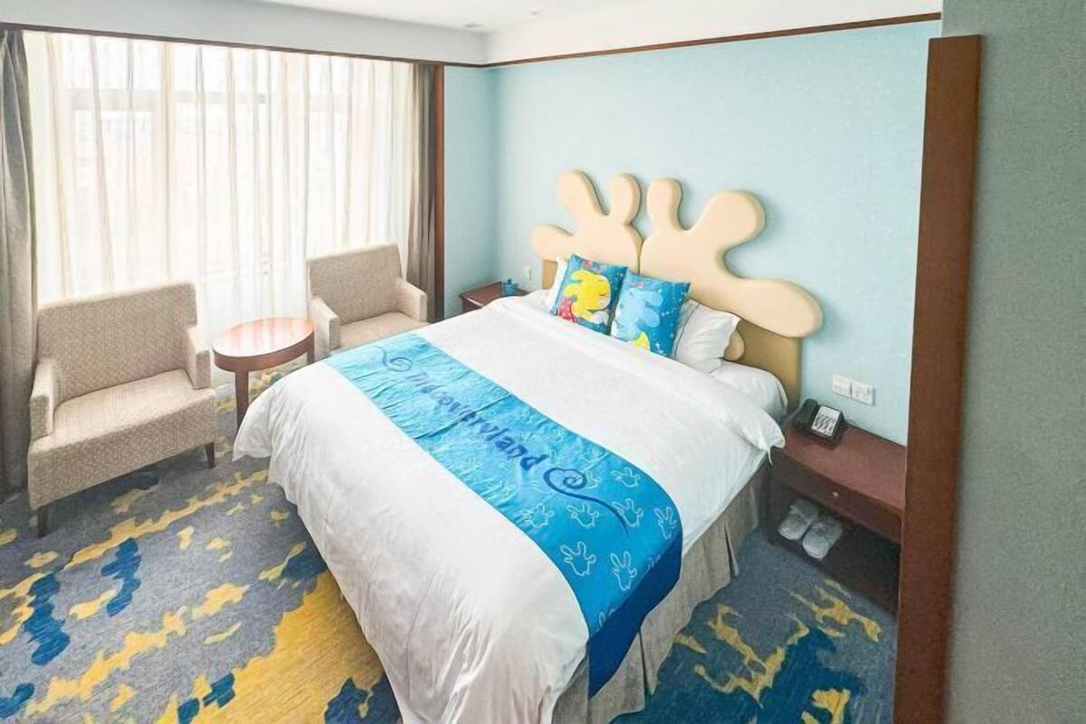 A hotel room with a large bed, two armchairs, a small round table, and a nightstand with a phone.