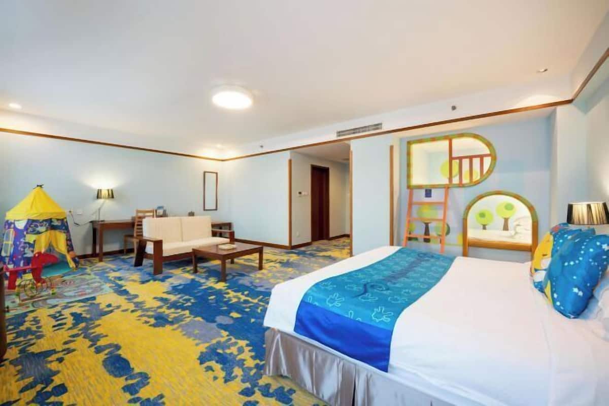 A hotel room with a large bed, a desk, a chair, and a small play area.