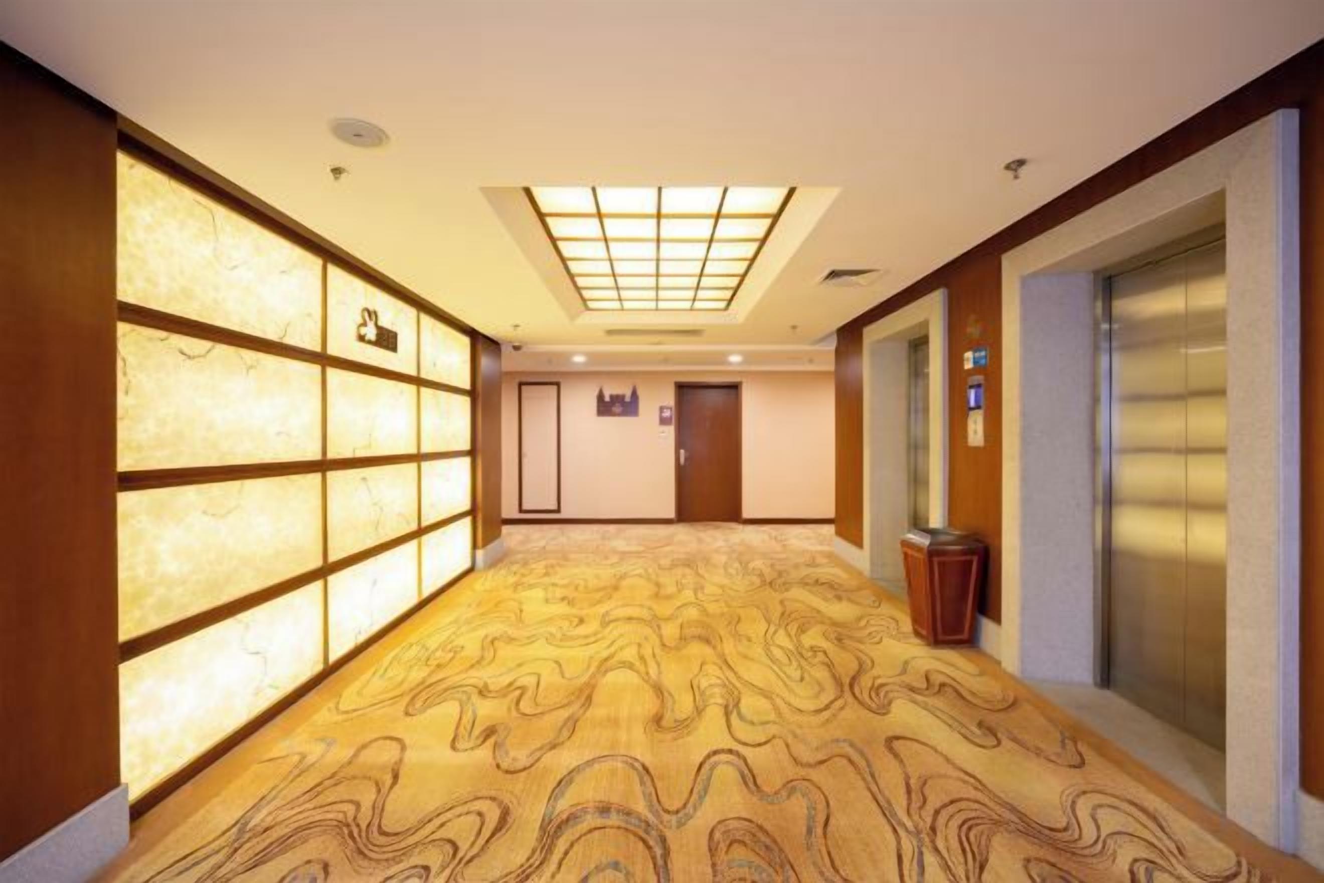 A hotel corridor with patterned carpet, a reception desk, and an elevator.