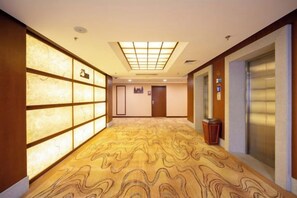 A hotel corridor with patterned carpet, a reception desk, and an elevator. - Discoveryland Hotel (Dalian)