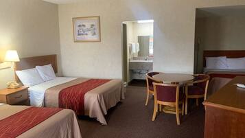 A hotel room with two beds, a desk, a chair, a small table, a lamp, and a painting on the wall.