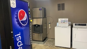 A vending machine with a Pepsi logo, a water dispenser, and two washing machines in a room with beige walls and a concrete floor. - Coachman's Inn Motel (Wynne)