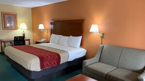 A hotel room with a bed, a grey sofa, a wooden coffee table, and two bedside lamps.