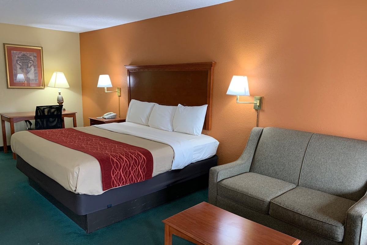 A hotel room with a bed, a grey sofa, a wooden coffee table, and two bedside lamps.