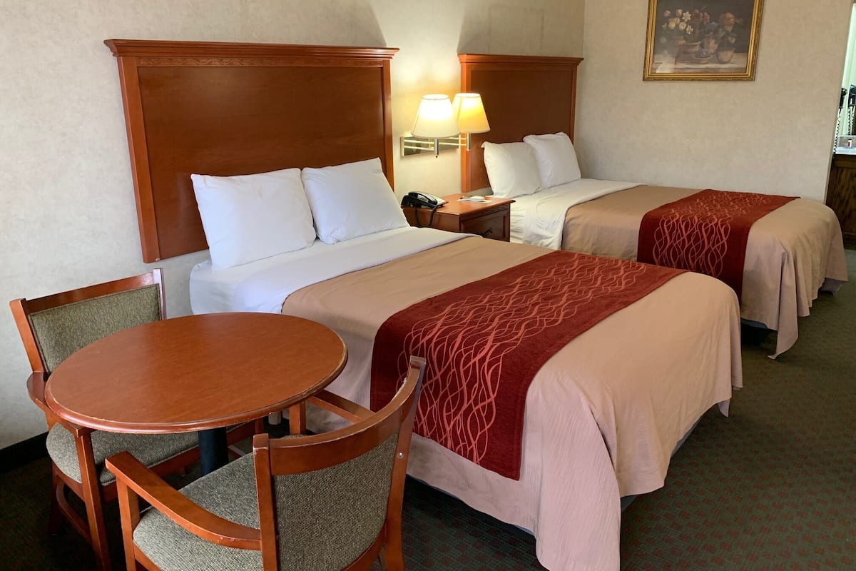 A hotel room with two beds, a wooden headboard, a round wooden table, and a chair.