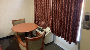 A small room with a round wooden table and two chairs, a white air conditioning unit, and a door with a red patterned curtain. - Coachman's Inn Motel (Wynne)