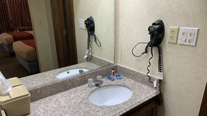 A bathroom with a granite countertop, two sinks, a mirror, and hair dryers mounted on the wall.