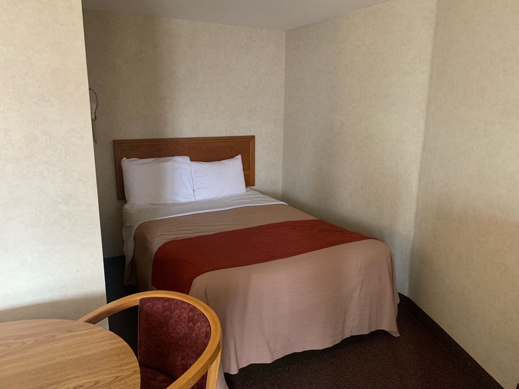 A small hotel room with a single bed, a wooden headboard, a red chair, and a small table.