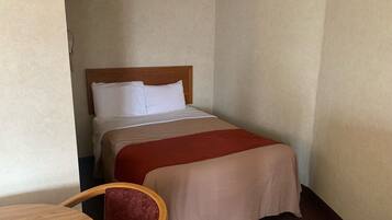 A small hotel room with a single bed, a wooden headboard, a red chair, and a small table.