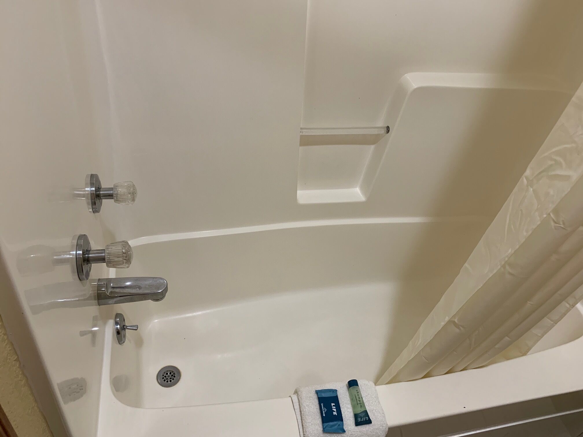 A white bathtub with a drain, two faucets, and a showerhead. There are two tubes of lotion on a towel.