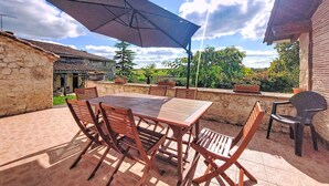 Eine Terrasse im Freien mit Tisch, Stühlen und einem großen Sonnenschirm, umgeben von Steinmauern.