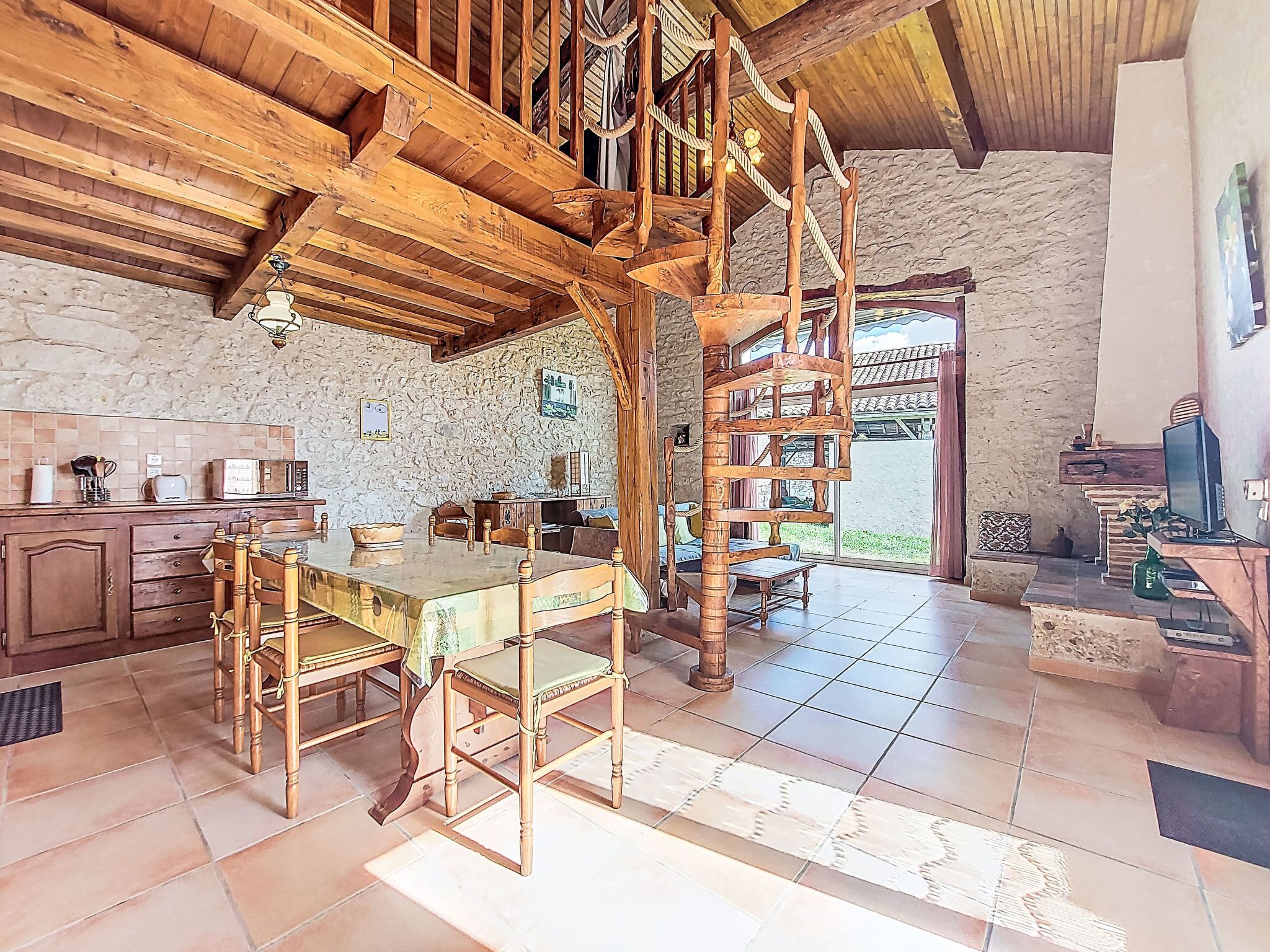 A rustic interior with a wooden staircase, a dining area with a table and chairs, and a kitchen with basic appliances.