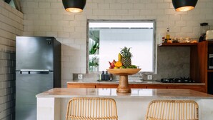 Una cocina con un refrigerador de acero inoxidable, una isla de madera con un frutero y sillas de mimbre.
