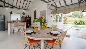 Cocina moderna con una isla central, zona de comedor con mesa redonda y sillas, y vista a una piscina exterior.