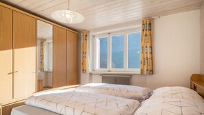 A bedroom with two beds, wooden wardrobe, window with curtains, and a radiator.
