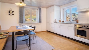 A modern kitchen with wooden flooring, a dining area with a table and chairs, a built-in oven, and a window with a view of the outdoors.