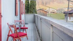 A balcony with a table and chairs, a wooden fence, and a view of houses and mountains.