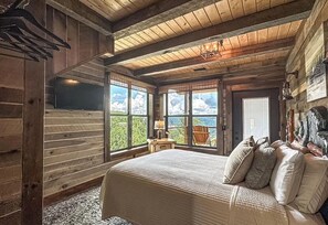 Een slaapkamer in een blokhut met een groot bed, houten wanden en uitzicht op de natuur.