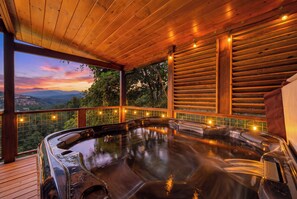 A hot tub on a wooden deck with a view of a sunset and mountains.