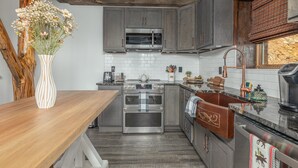 A kitchen with grey cabinets, a stainless steel oven, a microwave, and a wooden countertop.