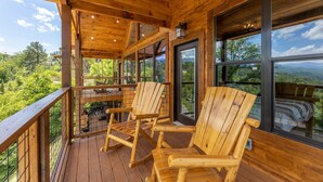 A wooden deck with Adirondack chairs, large windows, and a view of the mountains.