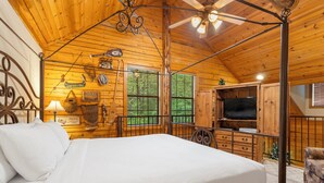 Ein Schlafzimmer einer Holzhütte mit einem Himmelbett, einem Deckenventilator und einem Fernseher.