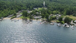 An aerial view of a lakeside community with boats docked along the shore, surrounded by dense forest. - Lake George House with Beautiful Lake Views and Lake Access 6 Bedrooms 14 People (Lake George)