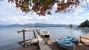 A wooden dock extending into a calm lake with boats docked at the end. - Lake George House with Beautiful Lake Views and Lake Access 6 Bedrooms 14 People (Lake George)