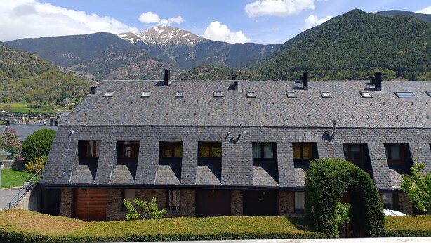 Un bâtiment doté d’un toit en pente, de nombreuses fenêtres et offrant une vue sur des montagnes en arrière-plan.