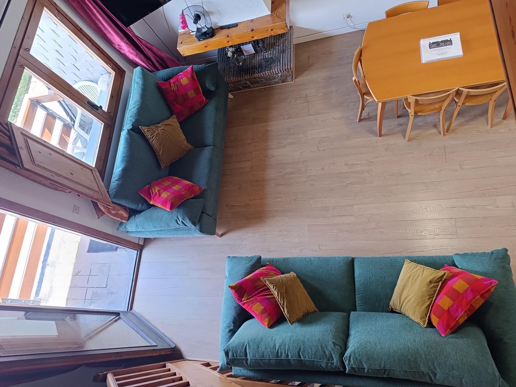 A living room with a teal sofa, wooden dining table, and a staircase.