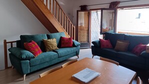 Un salon avec deux canapés de couleur turquoise, un plancher en bois, un escalier en bois et une grande fenêtre.