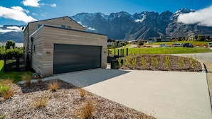 A modern two-story house with a large garage, surrounded by a landscaped garden and a mountain backdrop. - Jacks Point Family Retreat - Jacks Point Home (Queenstown)
