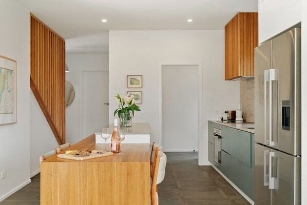 A modern kitchen with a wooden dining table, a refrigerator, and a small island with a vase of flowers.