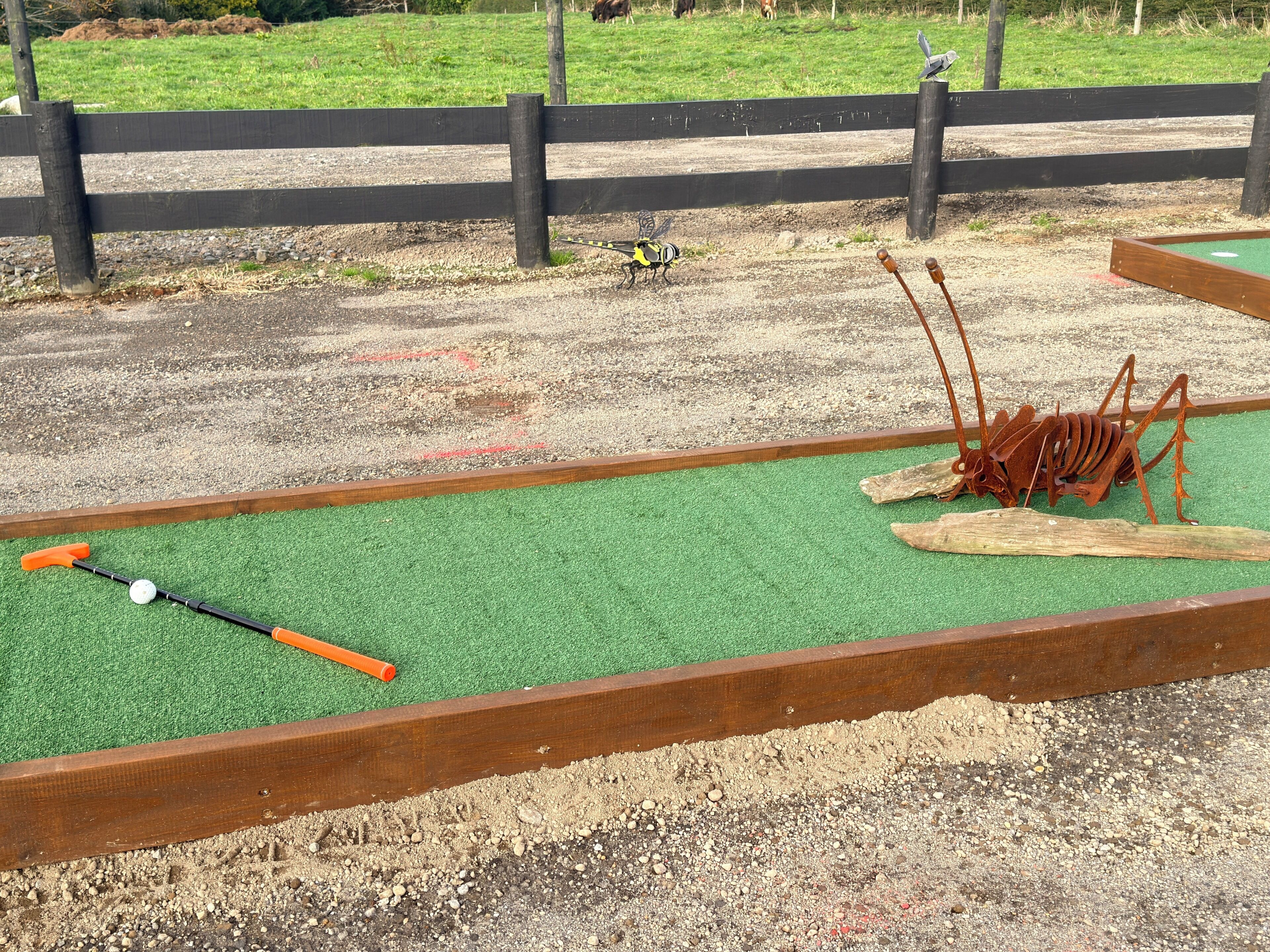 A miniature golf course with a green putting surface, a golf ball, and a putter.