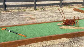 A miniature golf course with a green putting surface, a golf ball, and a putter.