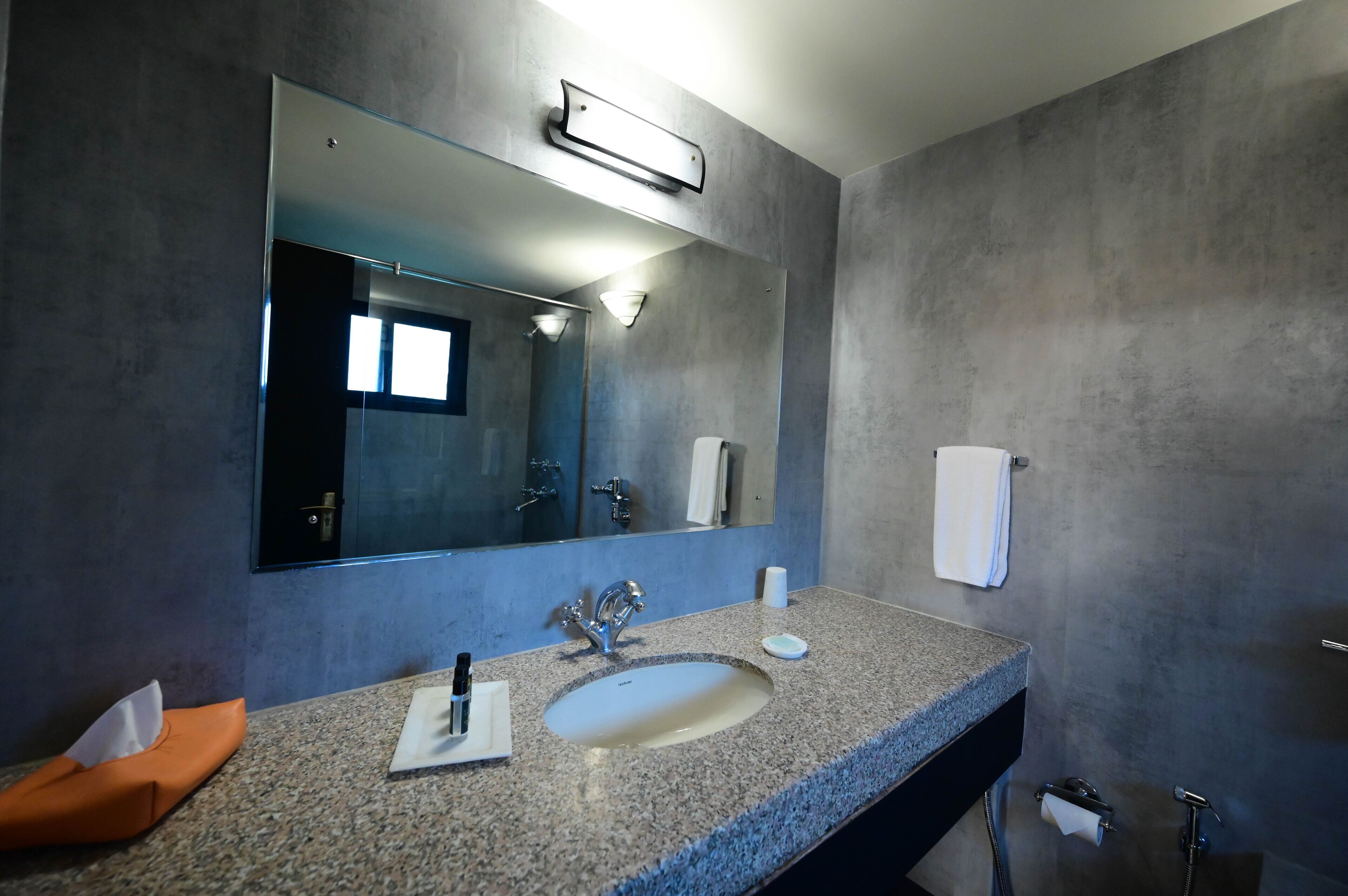 A modern bathroom with a granite countertop, a large mirror, a sink, a towel rack, and a shower area.
