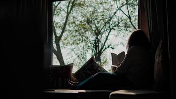 A person sitting by a window with a tree view, reading a book.