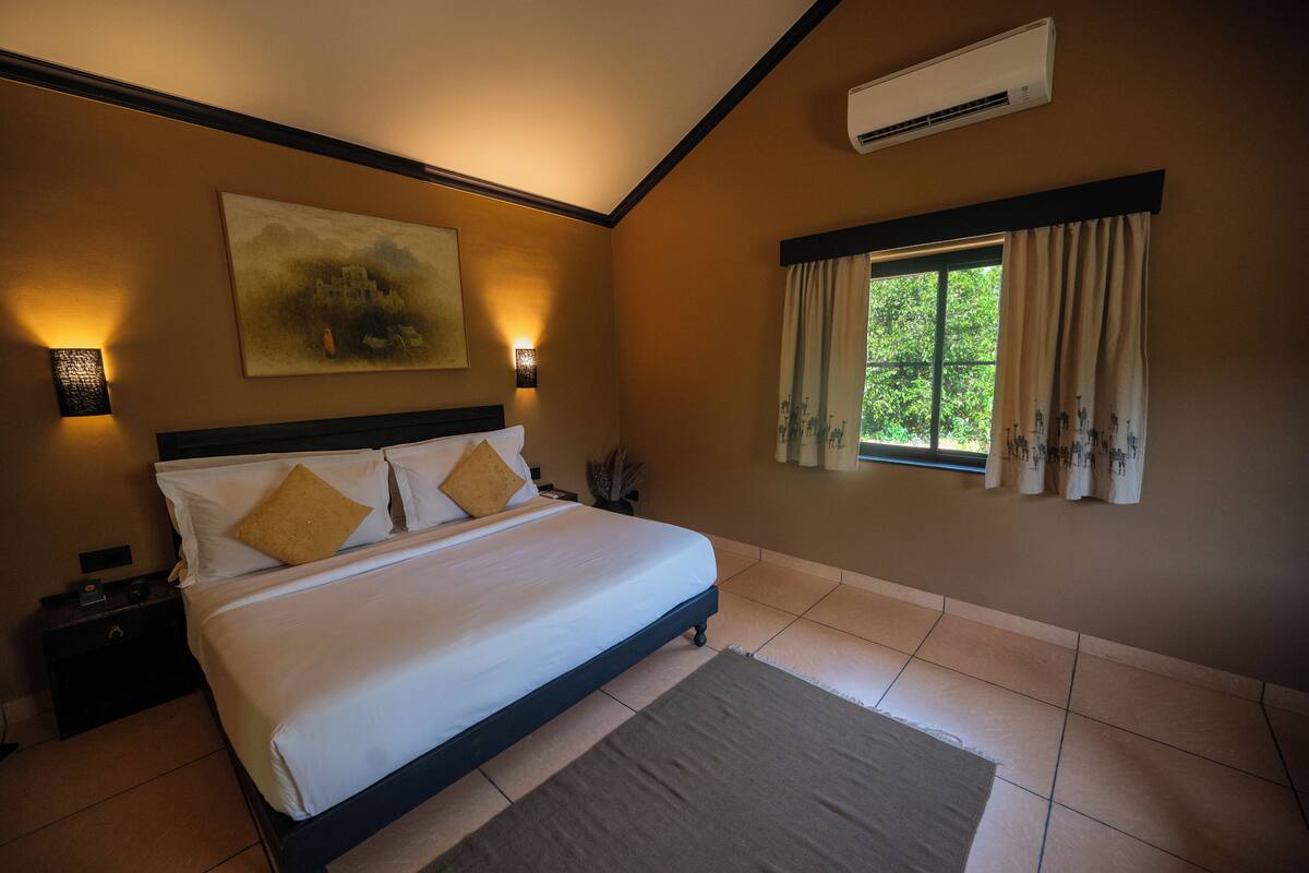 A bedroom with a large bed, a nightstand, a wall-mounted air conditioner, and a window with curtains.